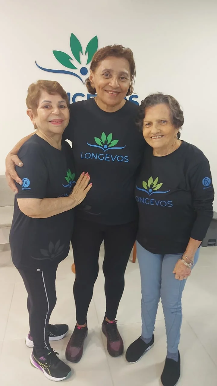 Três alunas reunidas diante da marca Longevos